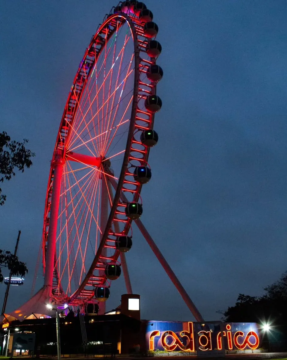 Roda-gigante inteira à noite, acesa em vermelho, com o letreiro iluminado na base.