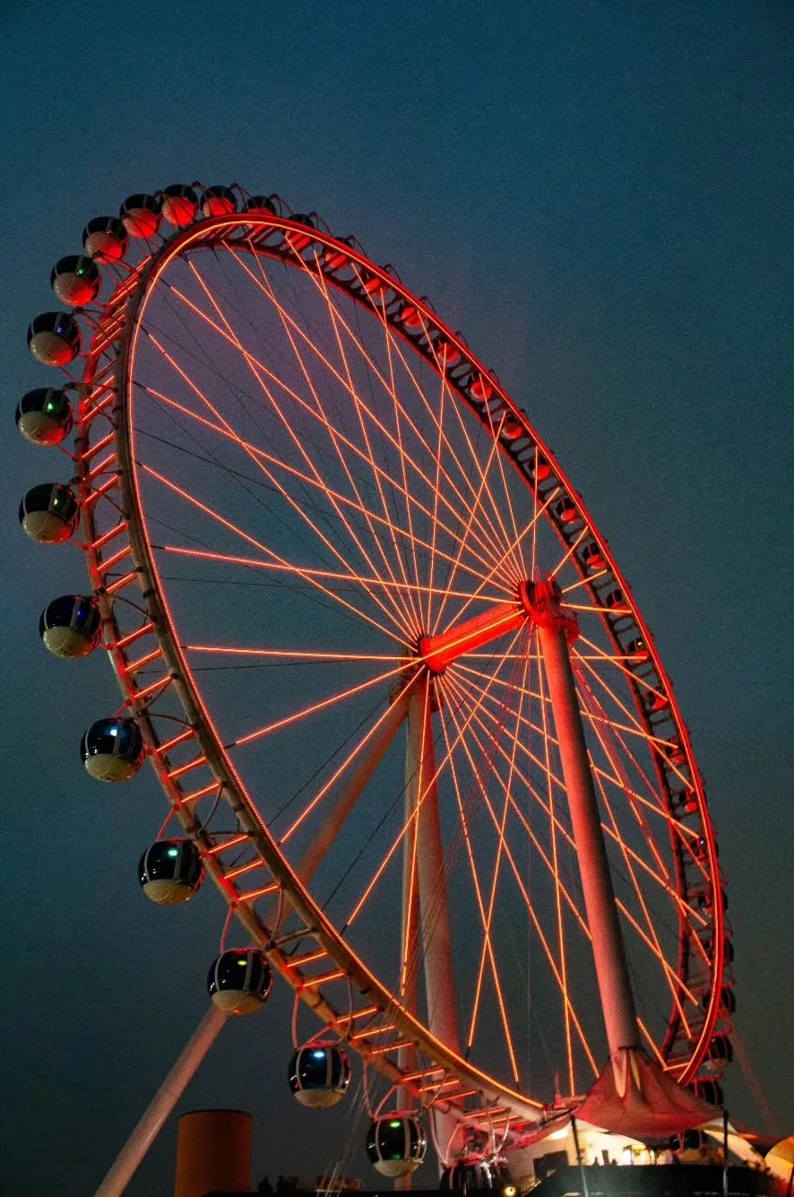 Roda-gigante acesa em vermelho contra o céu azul-escuro.