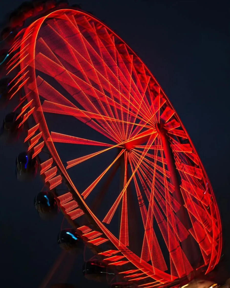 Raios da roda-gigante em vermelho intenso, de perto, no céu escuro.