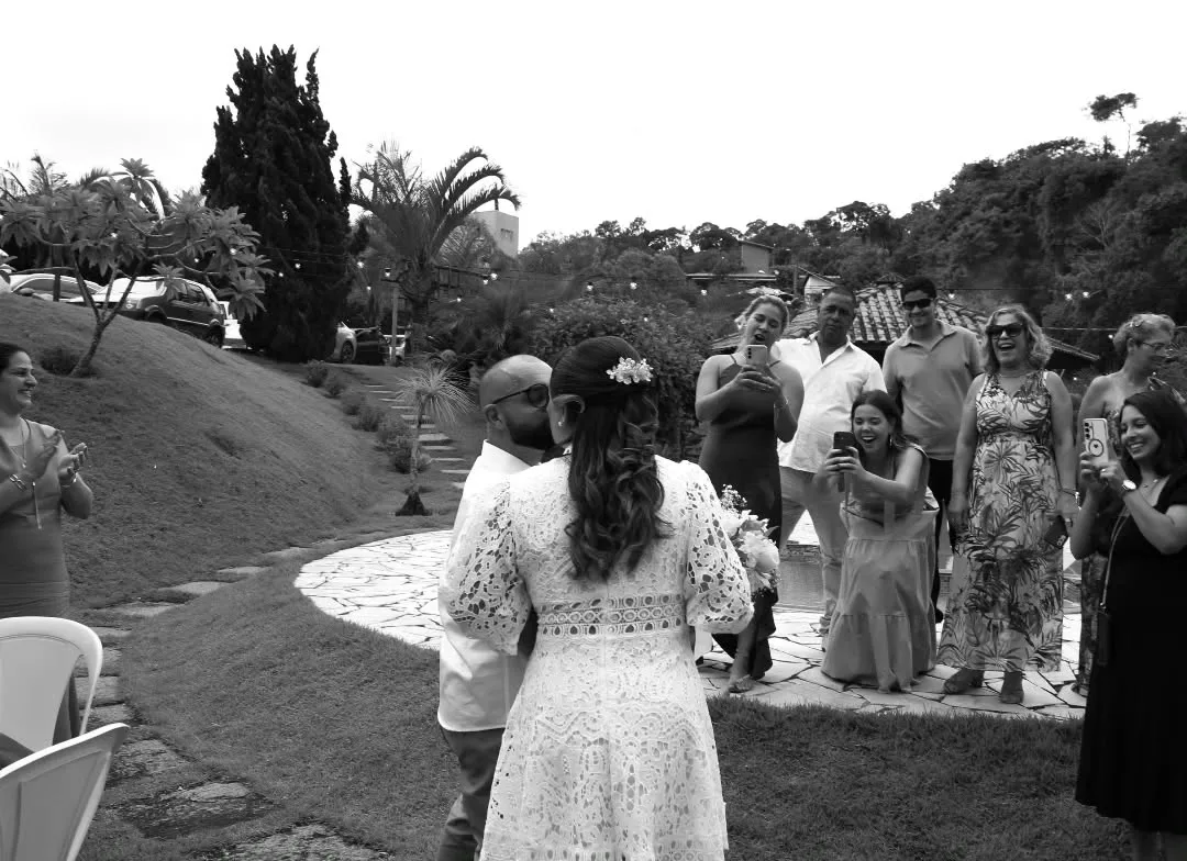 Noiva de costas caminha pelo jardim em direção aos convidados. Foto em preto e branco.